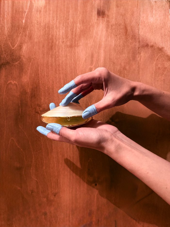 Hände mit blau gefärbten Fingerkuppen halten ein bernsteinfarbenes Objekt über Holz.